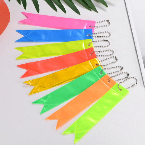8 Pack Reflective Safety Pendants With Chains For Backpacks, Running And Cycling, in fluorescent colors arranged on a table.
