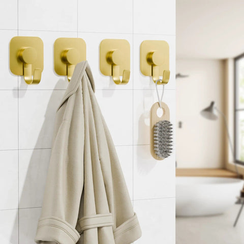 Heavy Duty Adhesive Wall Hooks In A Dope Four Pack, Stainless Steel Stick On Hangers With Badass Grip For Bathrooms And Kitchens, Waterproof And Super Fast To Put Up On Any Wall Or Door Without Drilling, Classic Gold Finish holding a coat on a tiled wall.