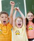 Children wearing school bus name tags in classroom with green chalkboards, showcasing 120 Pack School Bus Name Tags In 6 Cartoon Styles.