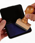 Hand holding wooden rubber stamp over Top Tier Fast Dry Ink Pad For Rubber Stamps And Crafting Projects.