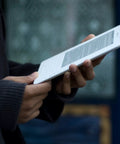 Person holding a sleek white second gen ereader with a sharp six inch screen, perfect for reading on the go.