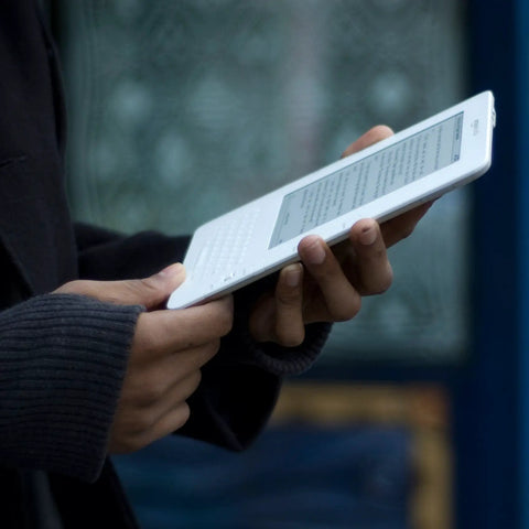 Person holding a sleek white second gen ereader with a sharp six inch screen, perfect for reading on the go.