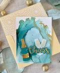 Handmade card with wine glasses and 'Cheers' on a decorative background with gold and blue accents.