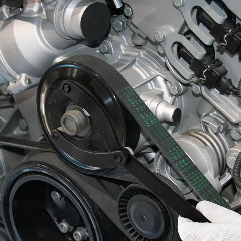 Pulley holder tool clamped on camshaft pulley in a car engine; black metal lever with timing belt and pulleys visible.