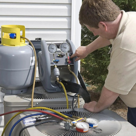 Man using HVAC gauges connected to AC unit for maintenance check outside a building