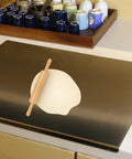 Front view of stainless steel kitchen cutting board with black surface; wooden rolling pin resting on a light-colored board.