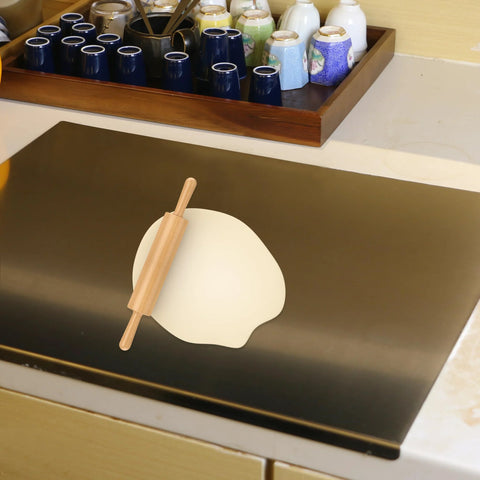 Front view of stainless steel kitchen cutting board with black surface; wooden rolling pin resting on a light-colored board.