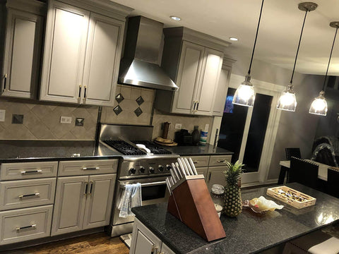 Modern kitchen with grey cabinetry, stainless steel appliances, and overhead pendant lighting. Knife block and serving tray on black countertops.