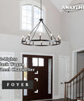 12-Light black wagon wheel chandelier in farmhouse foyer setting with high ceiling and windows.