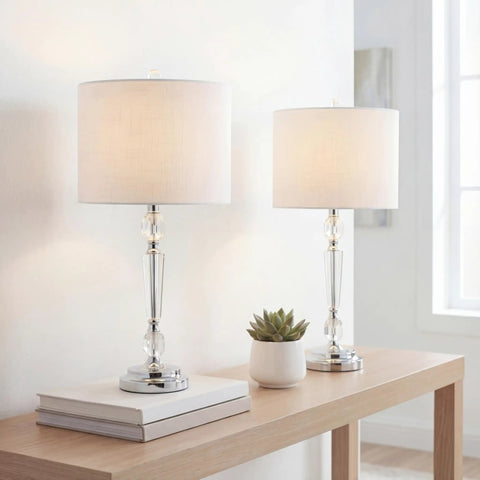 27 Inch Clear Crystal LED Table Lamp Set of 2 for Living Room or Bedroom on a wooden table, featuring chrome candlestick base and white linen shade.