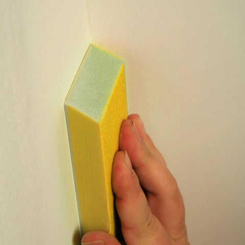 Hand using Very Fine 220 Grit Dual Angle Sanding Sponge 3 By 5 By 1 Inches for tight corner on wall