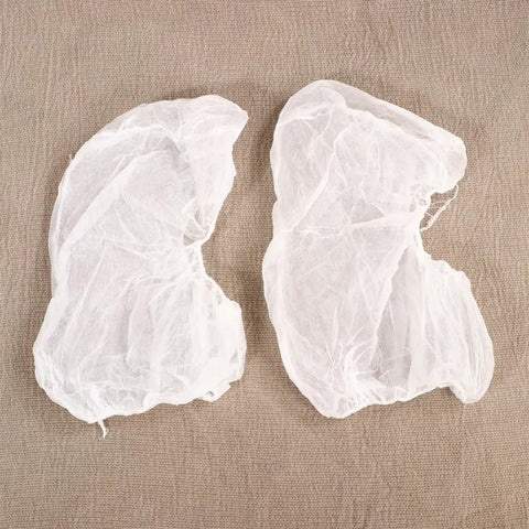 Straight Up Clean And No Drama Disposable Nonwoven Hair Covers With Tension Free Elastic Bands For Salon Beauty Chef Jobs And Long Daily Grind Sessions Pack Of 20 Fresh Caps, two white nonwoven hair covers on fabric.