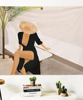 Artistic illustration of a woman in a black dress and straw hat relaxing on a sunbed with greenery.