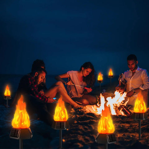 Group enjoying campfire surrounded by Solar Outdoor Torch Lights With Flickering Flame For Backyard And Garden Decor Waterproof LED Pathway Lanterns For Patio Yard And Camping Eight Pack Easy Auto On Off