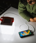 Your Go To Quick Inflate 2 In 1 Solar Lantern And Phone Charger illuminating a room, charging a phone with USB cable