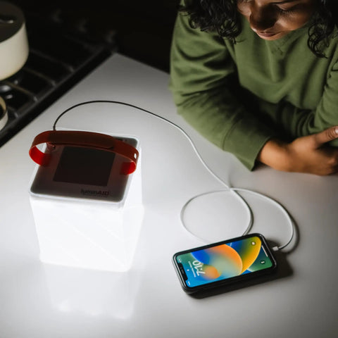 Your Go To Quick Inflate 2 In 1 Solar Lantern And Phone Charger illuminating a room, charging a phone with USB cable