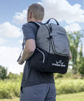 Man outdoors wearing Trooper Disc Golf Backpack Holds 18 Plus Discs, Lightweight Yet Tough Bag For Beginners, Black, Dynamic Discs logo