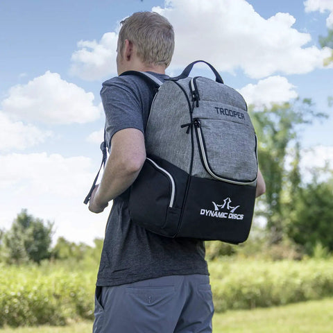 Man outdoors wearing Trooper Disc Golf Backpack Holds 18 Plus Discs, Lightweight Yet Tough Bag For Beginners, Black, Dynamic Discs logo