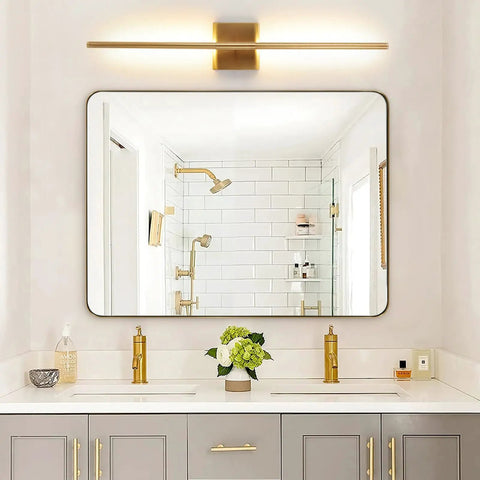 Bathroom vanity with gold fixtures, large mirror reflecting modern shower with white tiles, overhead gold bar light
