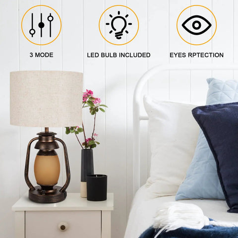 Bedroom setting with a Set Of 2 Farmhouse Table Lamps With Dual USB Charging Ports And 4 Way Rotary Switch, Rustic Metal Nightstand Lights, Beige Linen KD Fabric Drum Shade on a white nightstand, emphasizing warm ambient lighting and device charging convenience.