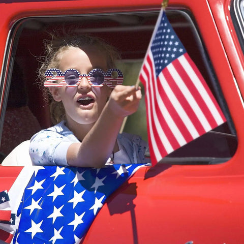 Child holding 8x12 Inch American Flag On Stick from 12 Pack With 17.5 Inch Wooden Poles during parade, showing vivid color.