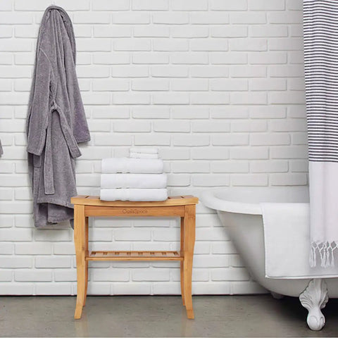 Bamboo Shower Bench 19 Inch Waterproof Shower Chair With Storage Shelf beside a bathtub, stacked with white towels.