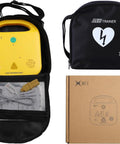 Front view of XFT AED trainer set: yellow trainer in black backpack case with mesh pocket and cardboard box.