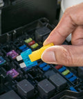 Hand holding a blue automotive blade fuse with yellow puller tool to replace in a fuse box, Snag This Straight Shooting 60 Piece Automotive Blade Fuse Kit With Sturdy Puller Tool For Cars Rv Trucks Motorcycles Heavy Duty 12V 24V Assortment That Knocks Out Shorts Quick No Sweat.