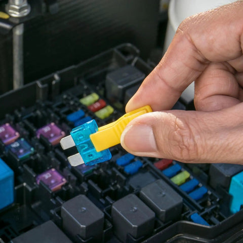 Hand holding a blue automotive blade fuse with yellow puller tool to replace in a fuse box, Snag This Straight Shooting 60 Piece Automotive Blade Fuse Kit With Sturdy Puller Tool For Cars Rv Trucks Motorcycles Heavy Duty 12V 24V Assortment That Knocks Out Shorts Quick No Sweat.