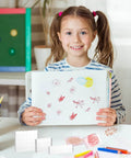 Child holding artwork with Six Clear Acrylic Stamp Blocks Set With Grid Lines For Easy Stamping Crafting And Scrapbooking visible on table.