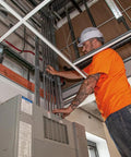Construction worker in orange shirt adjusting wiring in a building ceiling.