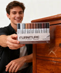 Person holding 12 Color Wood Marker Set For Furniture Repair next to scratched wooden cabinet for touch up of surfaces.
