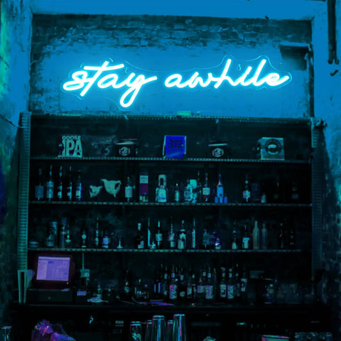 Pink Stay Awhile Neon Sign LED Dimmable Bar Light for Wall Decor USB Powered Cool Neon Light in a dimly lit blue-themed bar.