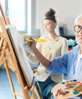 Two women painting indoors; one using a roller from the Premium Top Shelf Paint Roller And Bristle Brush Kit With Heavy Duty No Drip Tray Plus Ultra Soft Sponge Rollers For Smooth Wall Coating And No Sweat Weekend Projects.