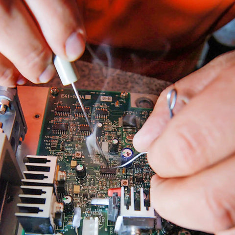 Hands using tin lead solder wire kit with rosin paste flux on a circuit board, illustrating electrical soldering process.