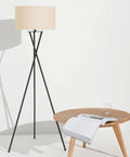 LED Floor Lamp Tall Tripod With Drum Shade In Black Finish And Gold Accents next to wooden table, modern living room decor