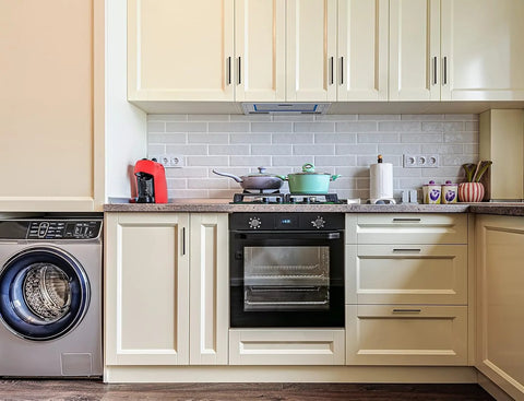 Modern kitchen with cream cabinets, integrated oven, washing machine, and counter appliances, featuring sleek drawer handles.