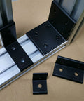Badass Aluminum Corner Braces For 4080 Extrusion Profiles With Eight Predrilled Holes In Matte Black Finish Pack Of Four positioned on shelving.