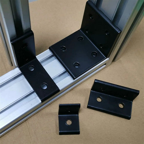Badass Aluminum Corner Braces For 4080 Extrusion Profiles With Eight Predrilled Holes In Matte Black Finish Pack Of Four positioned on shelving.