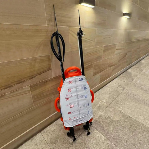 Spearfishing Float Buoy With Foldable Carbon Fiber Flagpole And D Ring Handles Built In Fish Measuring Ideal For Freediving Snorkeling Rescue And Underwater Sports Orange Red in a tiled corridor.
