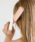 Woman using a hairbrush with a white nitrile finger sleeve for grip, showcasing hair care technique.