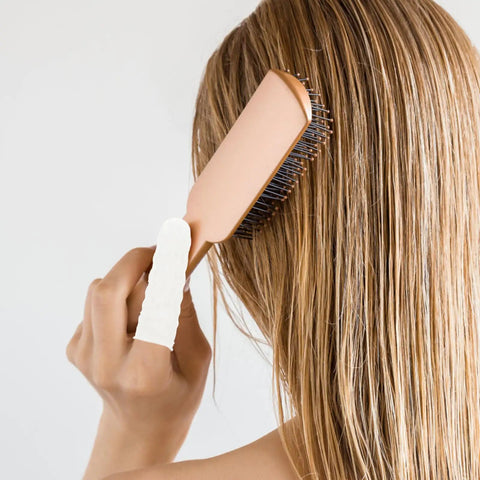 User brushing hair with a rose gold paddle brush, showing smooth strands and a white finger cot for grip.