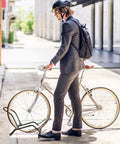 Commuter in suit parking bike in Two Pack Bike Floor Stand For Mountain And Road Bicycles, Fits 20 To 29 Inch Wheels, 23C To 4.0 Inch Wide Tires, Indoor Outdoor Bike Rack, Easy Push On Parking For Front Or Rear Wheel, Black.