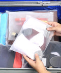 Hands holding a frosted zip-lock bag containing clothes, part of a 30 Pack Transparent Reusable Clothes Storage Bags With Zip Lock for Travel and Storage Grab and Go Durable Frosted Waterproof Organizers for Clothes Shoes Cosmetics and Essentials, inside a suitcase.