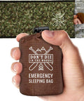 Man holding compact Emergency Sleeping Bag With Hood For Cold Weather Survival Dope Extra Thick Thermal Mylar Blanket in camo design.
