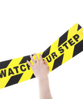 Two Pack Watch Your Step Floor Stickers Anti Slip Safety Decal 6X24 Inch Heavy Duty abrasive grip tape being held.