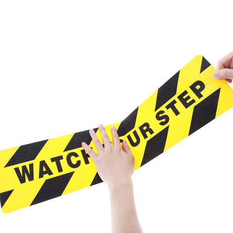 Two Pack Watch Your Step Floor Stickers Anti Slip Safety Decal 6X24 Inch Heavy Duty abrasive grip tape being held.