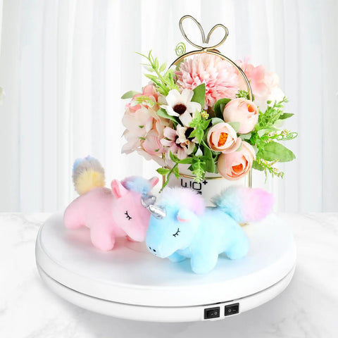 Tuanse 10 Inch Electric Motorized Rotating Turntable Cup Display Stand With Led Light showcasing plush unicorns and flowers on a white base.