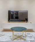 Modern living room with wall-mounted TV, white console, and round glass coffee table with gold legs on patterned rug.