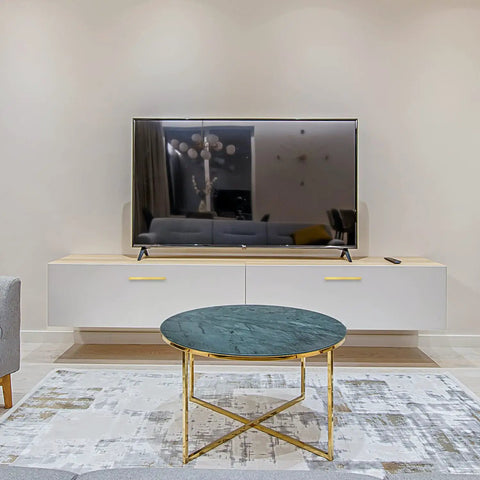 Modern living room with wall-mounted TV, white console, and round glass coffee table with gold legs on patterned rug.